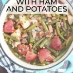 Green beans with ham and potatoes in a Dutch oven with a napkin, wooden spoon, and a few sprigs of parsley to the side.