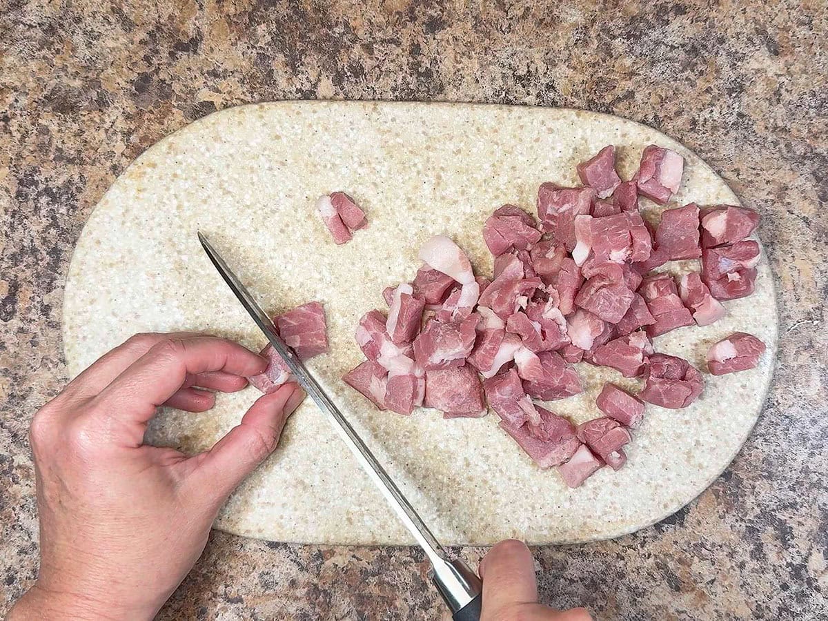Hands using a sharp knife to dice the country ham on a cutting board.