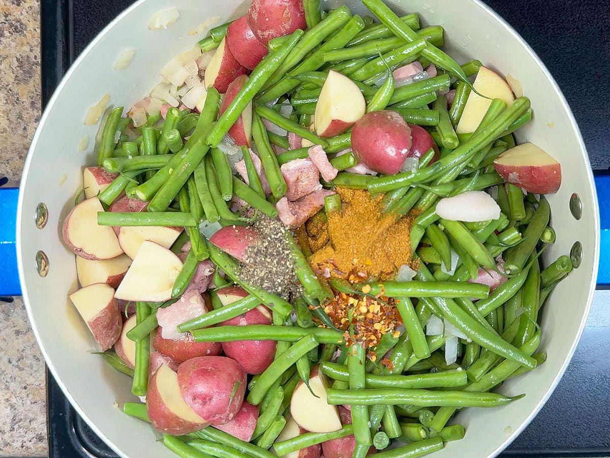 Adding red pepper flakes to the pot with the ground black pepper, Cajun seasoning, potatoes, ham, and vegetables.