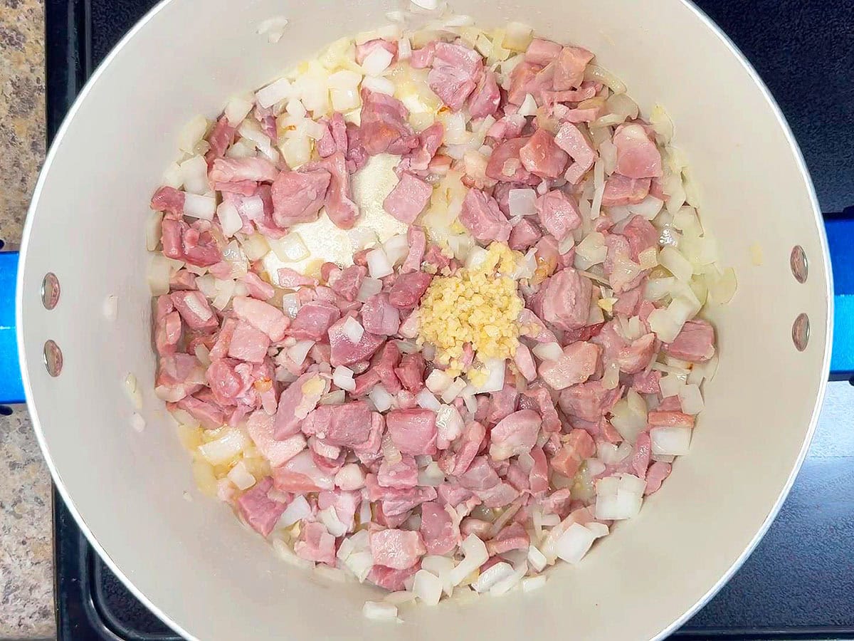 Minced garlic added to the cooked diced onions and country ham in a large stock pot.
