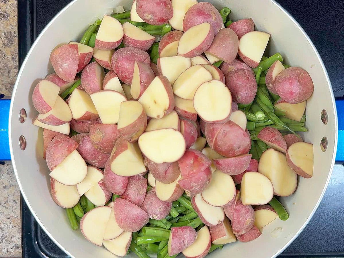 Adding chopped red potatoes to the pot with the green beans, country ham, diced tomatoes and garlic.