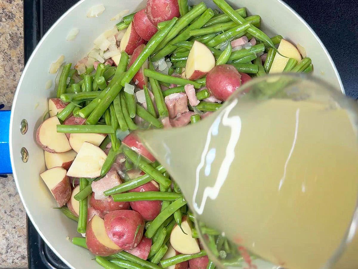 Pouring chicken broth over the diced ham and vegetables.