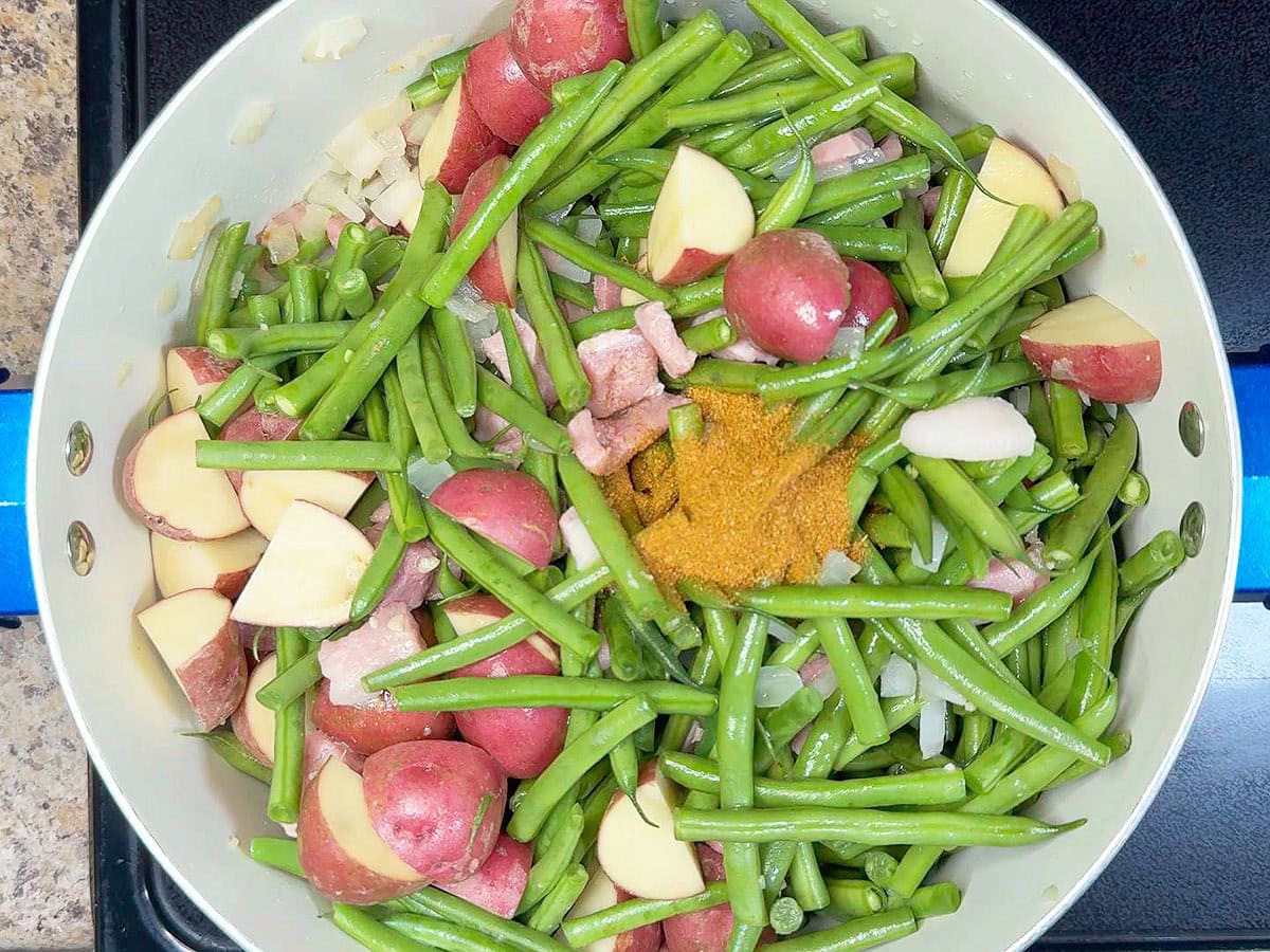 Adding Cajun seasoning to the pot with the potatoes, ham and vegetables.