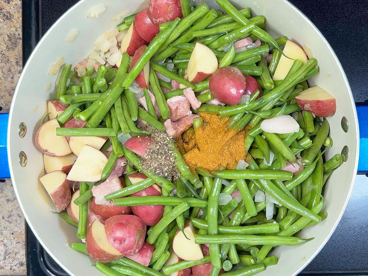 Adding ground black pepper to the pot with the Cajun seasoning, potatoes, ham, and vegetables.