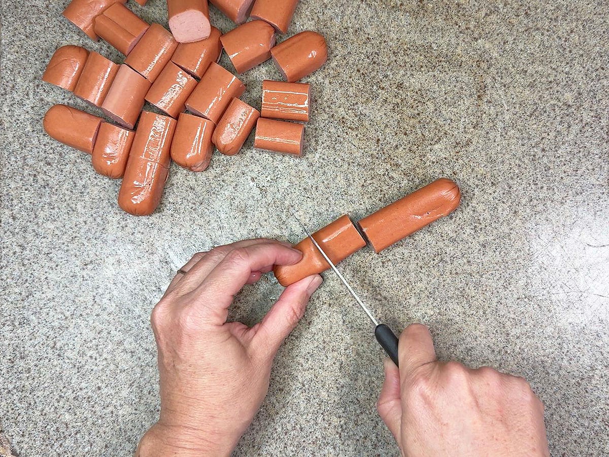 Hands using a paring knife to cut hot dogs into smaller pieces.