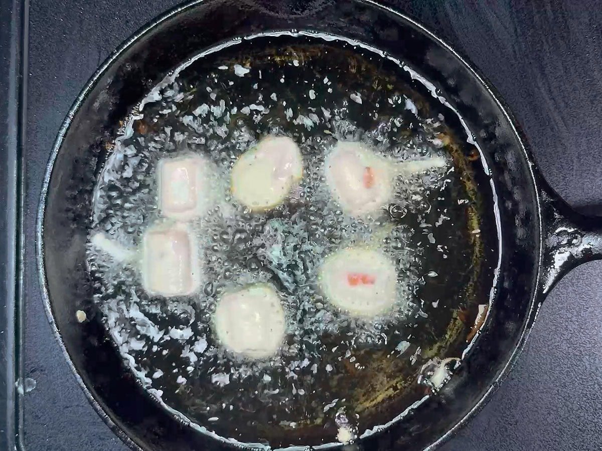 Frying the mini corn dog bites in hot oil in a cast iron skillet.