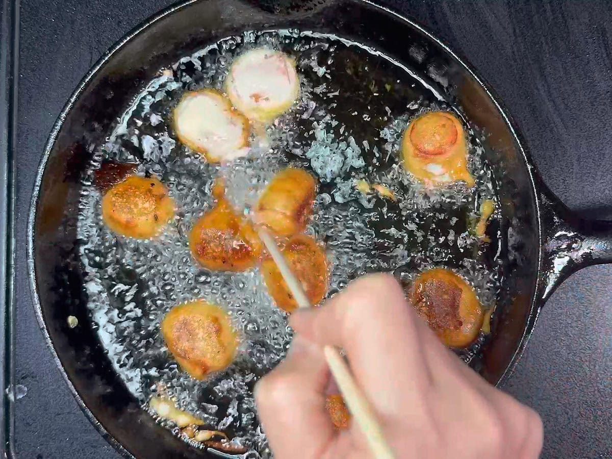 Using a wooden skewer to flip the mini corn dog pieces over in the hot oil.