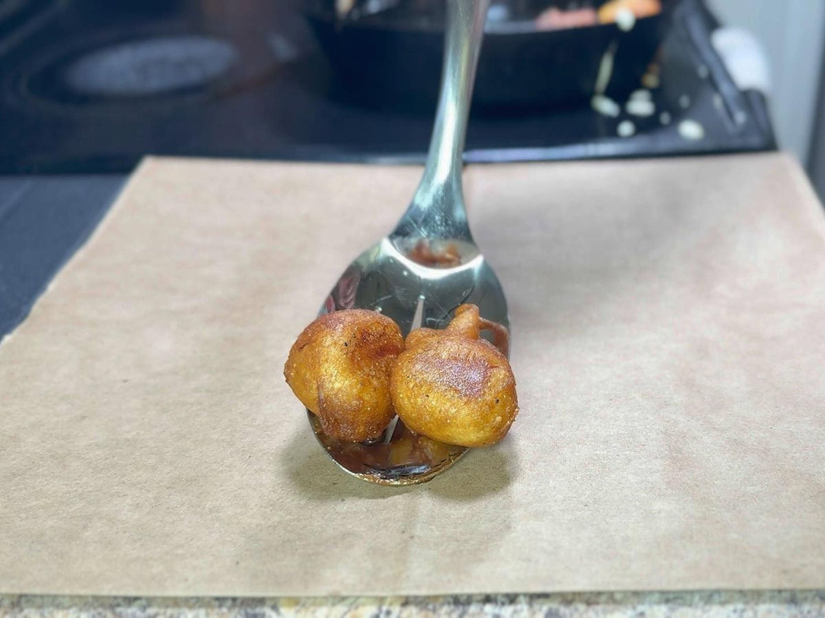 Removing the mini corn dog bites with a slotted spoon onto a brown paper sack.
