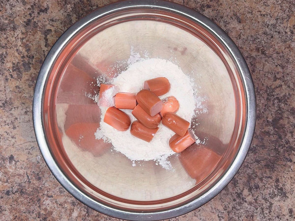 Adding hot dog pieces to the flour.