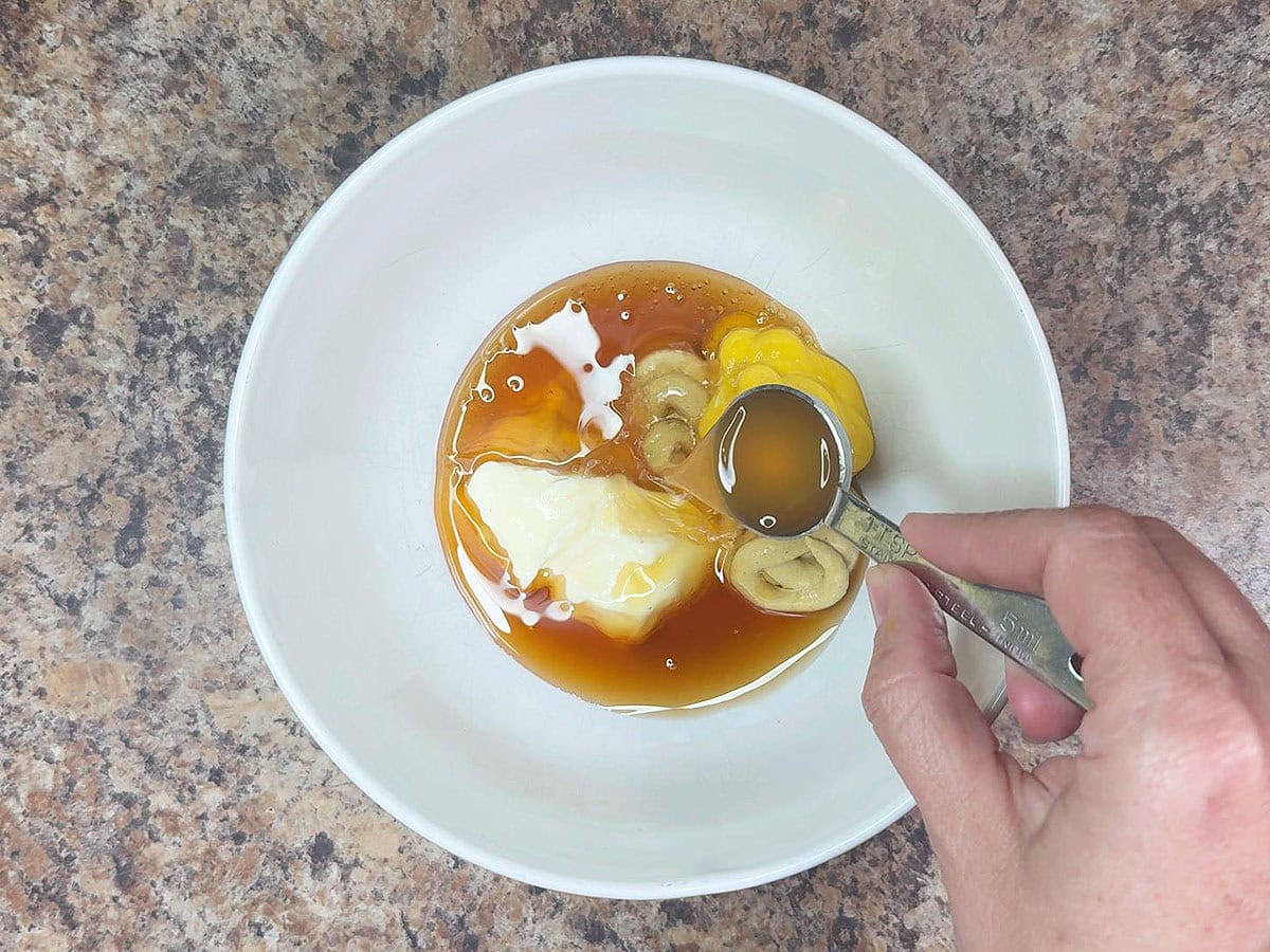 Adding apple cider vinegar to the mayonnaise, Dijon mustard, yellow mustard, and honey in a mixing bowl.