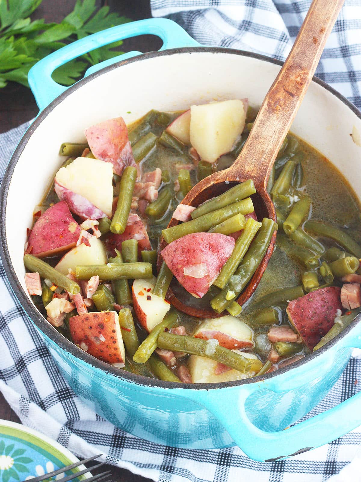 Rustic wooden spoon dishing up a serving of green beans with ham and potatoes.