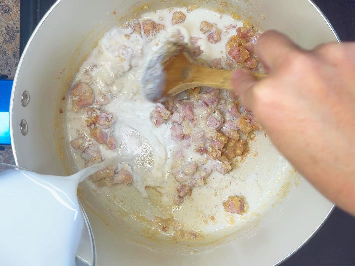 Stirring milk into the pot with the flour, garlic, and ham.