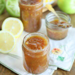 Jars of green tomato jam surrounded by sliced lemons and whole green tomatoes.