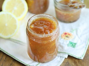 Jar of green tomato jam surrounded by sliced lemons and whole green tomatoes.