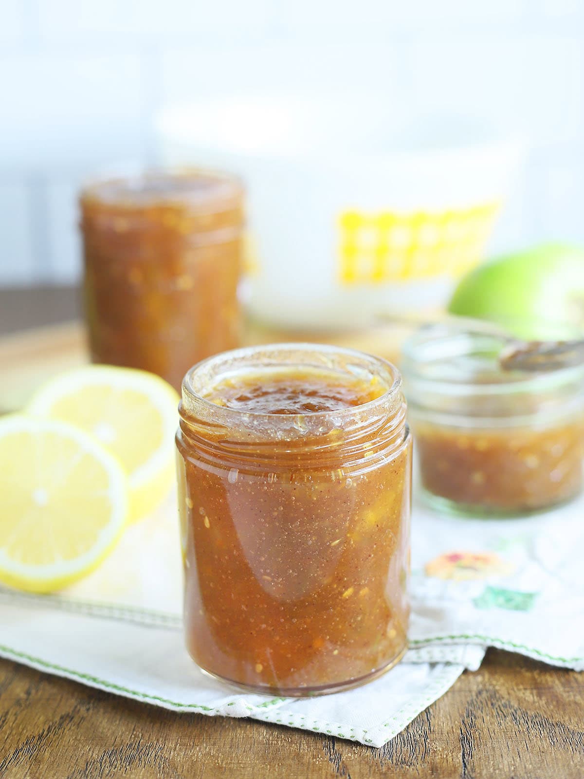 Jars of green tomato jam surrounded by sliced lemons and whole green tomatoes.