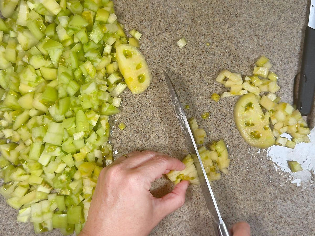 Hands using a knife to dice green tomatoes on a stone cutting board.
