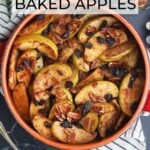 Baked apples garnished with raisins and pecans in a round clay serving dish. Smaller dishes of baked apples, a whole Granny Smith apple, a dish of brown sugar, pecans, and a measuring cup of raisins to the side.