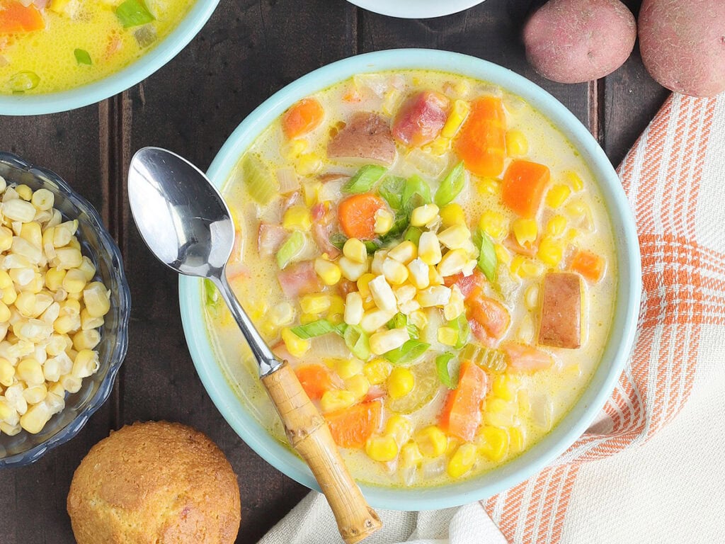 Dish of potato corn chowder with a spoon resting on the rim and a napkin to the side.