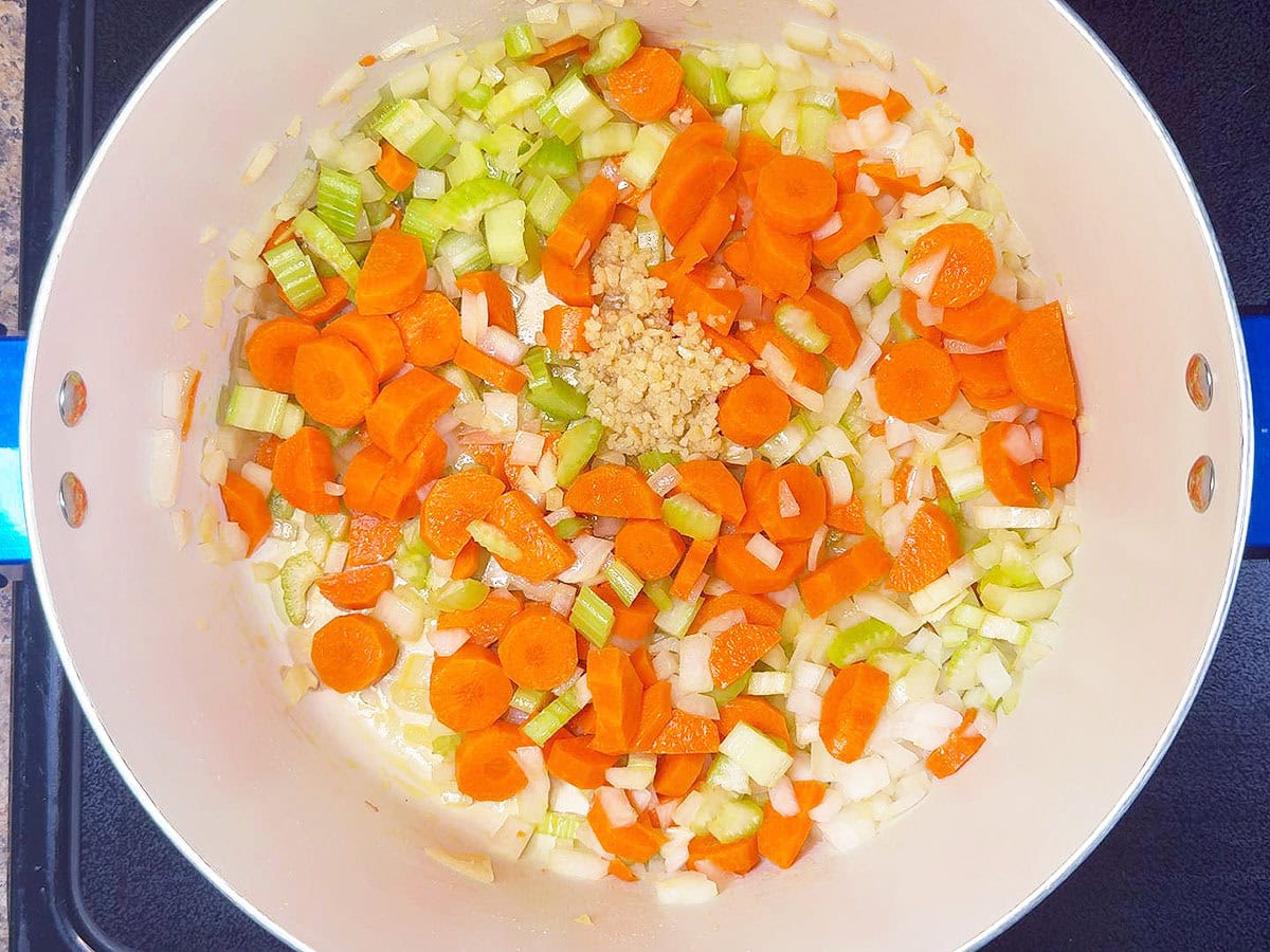 Sauteing diced carrots, celery, onions, and minced garlic in a large stock pot.