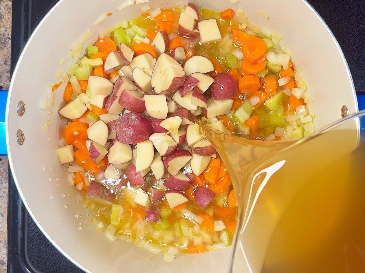 Adding potatoes and chicken stock to the pot with the carrots, celery, and onions.