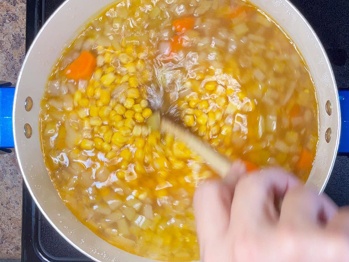 Stirring corn into the pot of potato corn chowder.