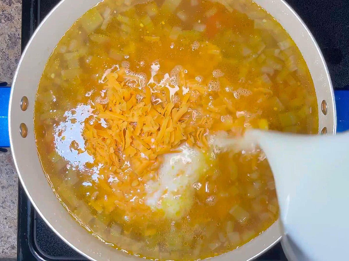 Adding cheese and milk to the pot of potato corn chowder.