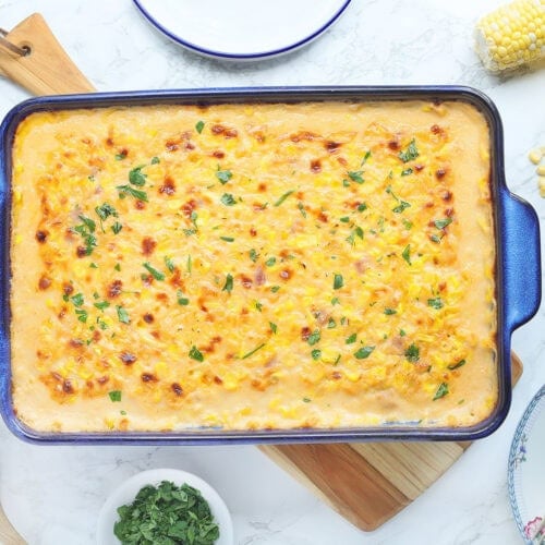 Baked cheesy corn casserole garnished with parsley in a rectangular baking dish.