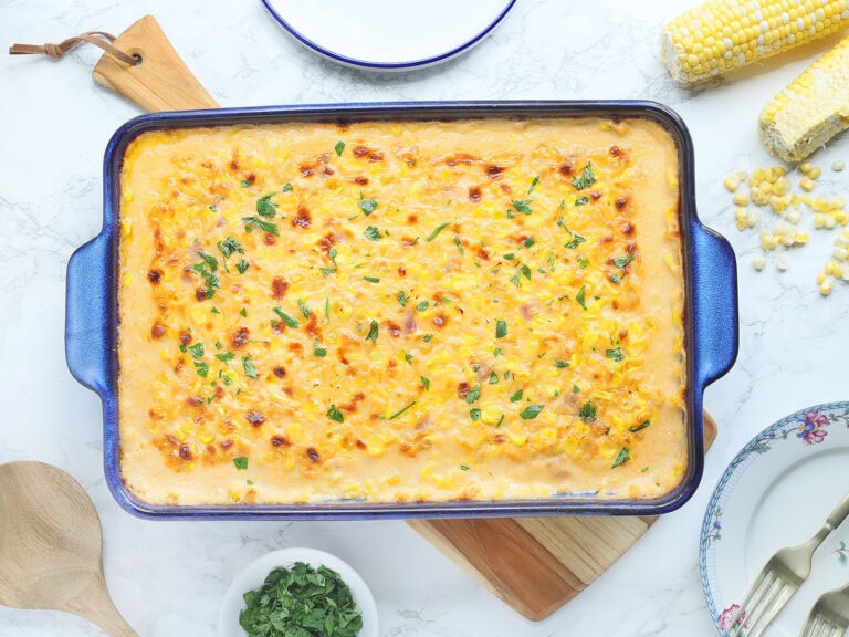 Baked cheesy corn casserole garnished with parsley in a rectangular baking dish.