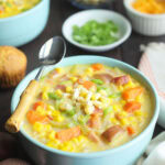 Two bowls of potato corn chowder with dishes of green onions, corn and cheese to the side.