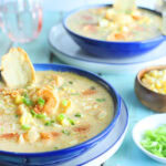 Two bowls of shrimp and corn bisque garnished with corn kernels and toasted bread.