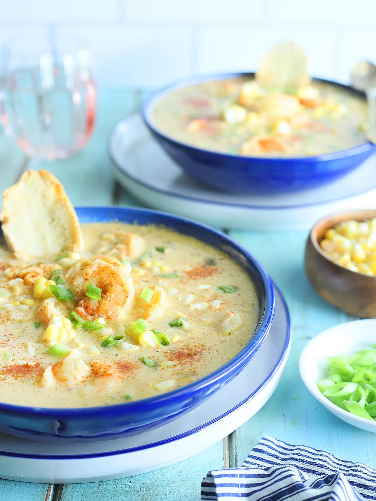 Two bowls of shrimp and corn bisque garnished with corn kernels and toasted bread.