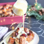Pouring rum creme anglaise over the top of a slice of white chocolate cranberry bread pudding.