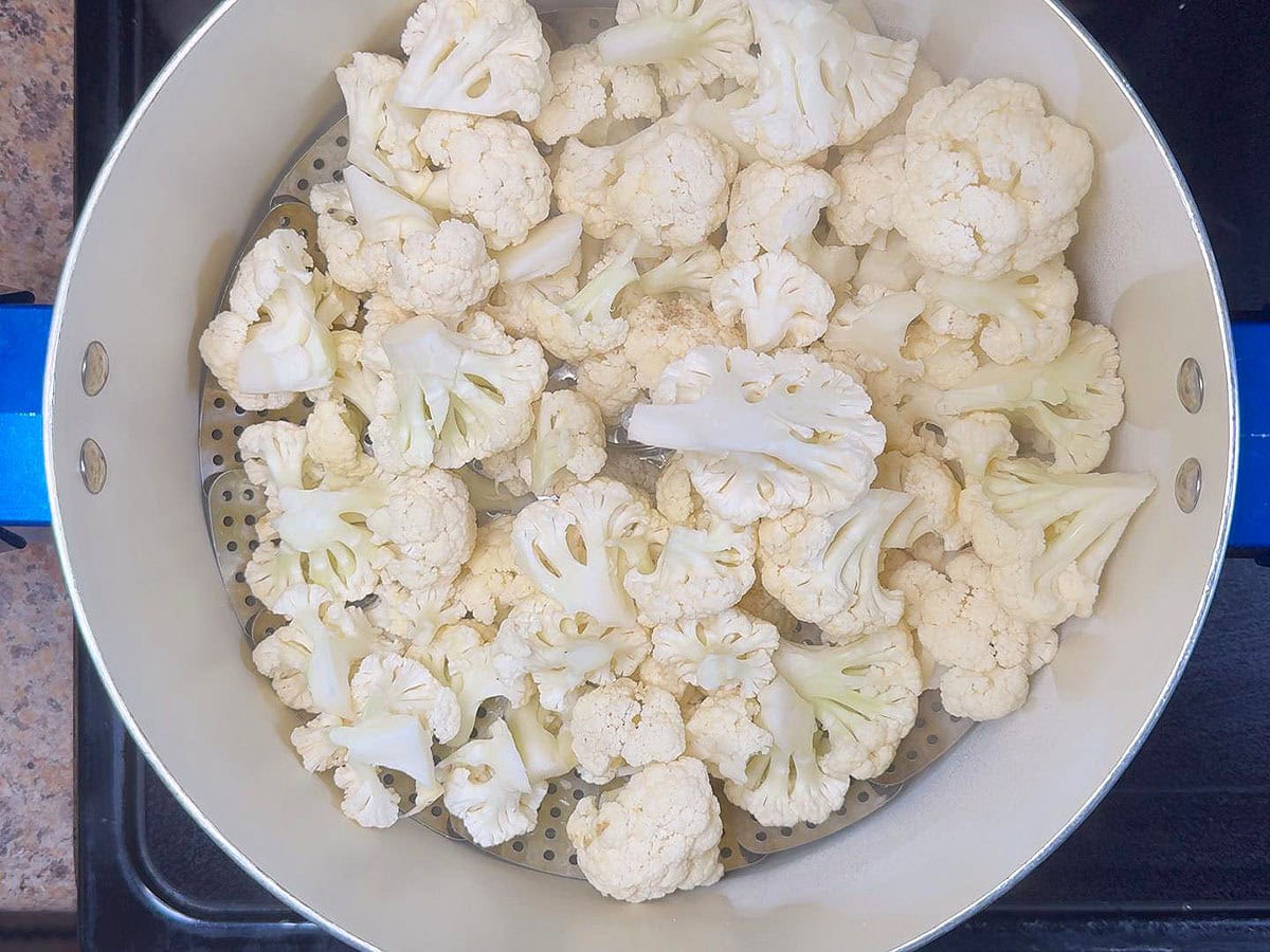 Cauliflower florets in a steam basket placed in a large stockpot.