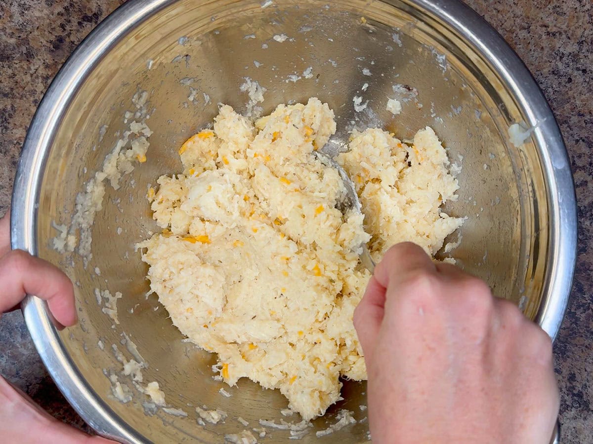Mixing Parmesan cheese, Colby-Monterey Jack cheese, unsalted butter, garlic powder, Montreal steak seasoning, dried thyme leaves, and salt and pepper into the cooked and mashed cauliflower florets.
