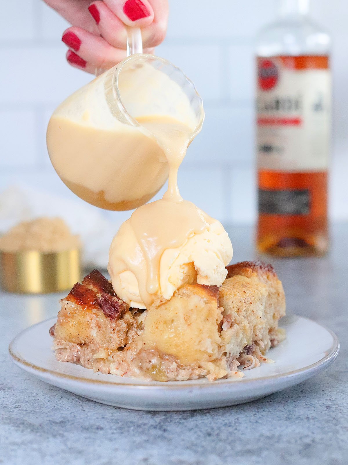 Pouring the rum sauce over a sliced of bread pudding topped with ice cream.