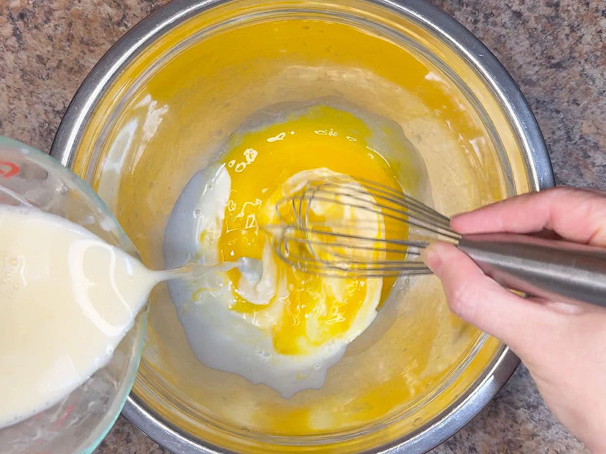 Tempering the mixture by adding warm cream to the egg yolks.