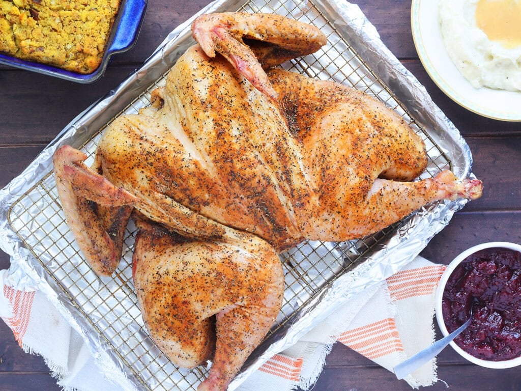 Smoked spatchcocked turkey resting on a rack on a foil lined baking sheet.