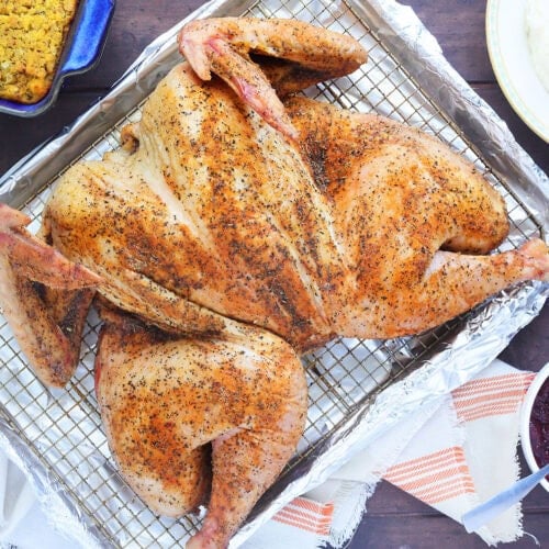 Smoked spatchcocked turkey resting on a rack on a foil lined baking sheet.