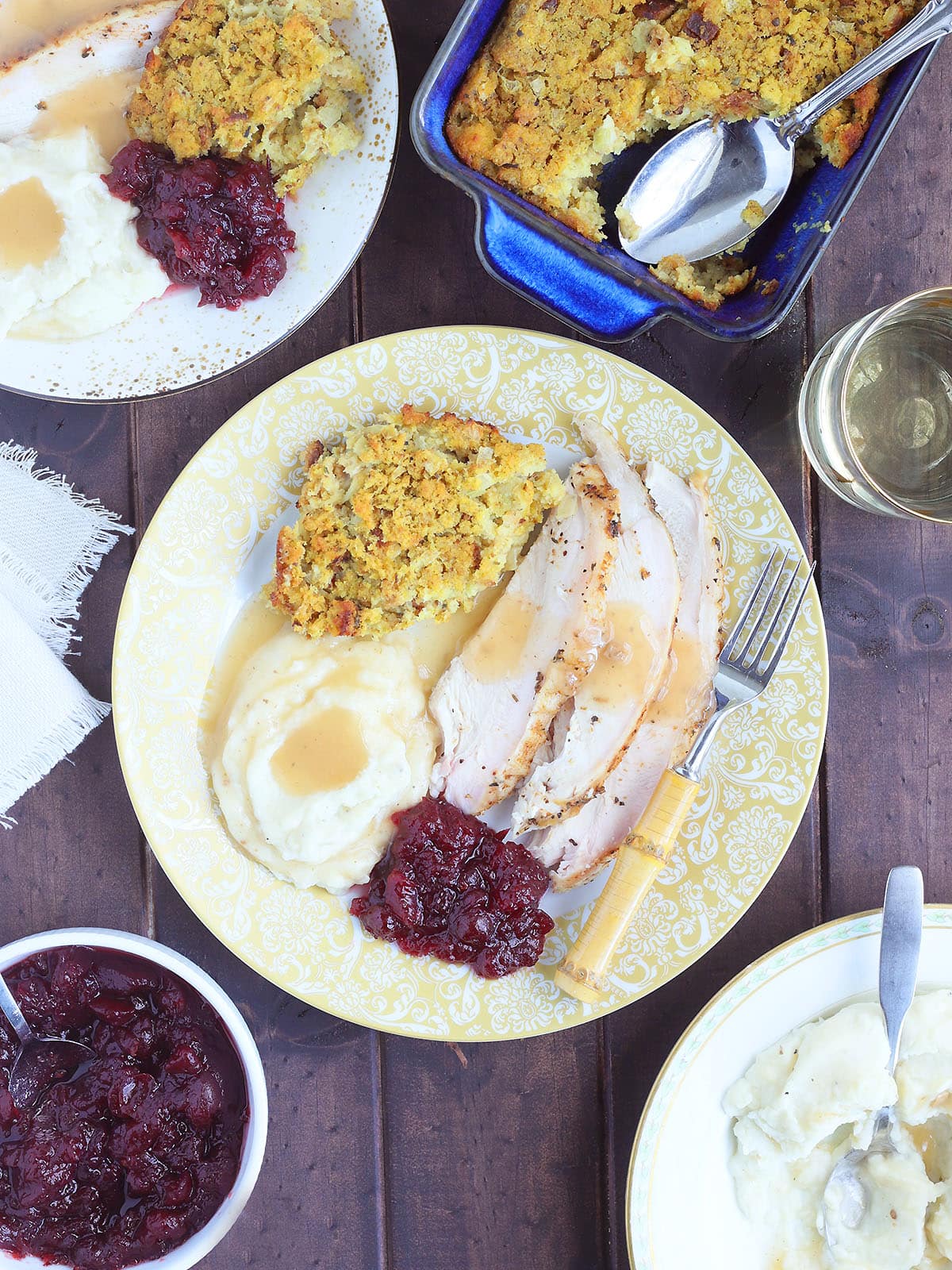 Sliced smoked spatcocked turkey on a plate with mashed potatoes, cornbread dressing and cranberry sauce.