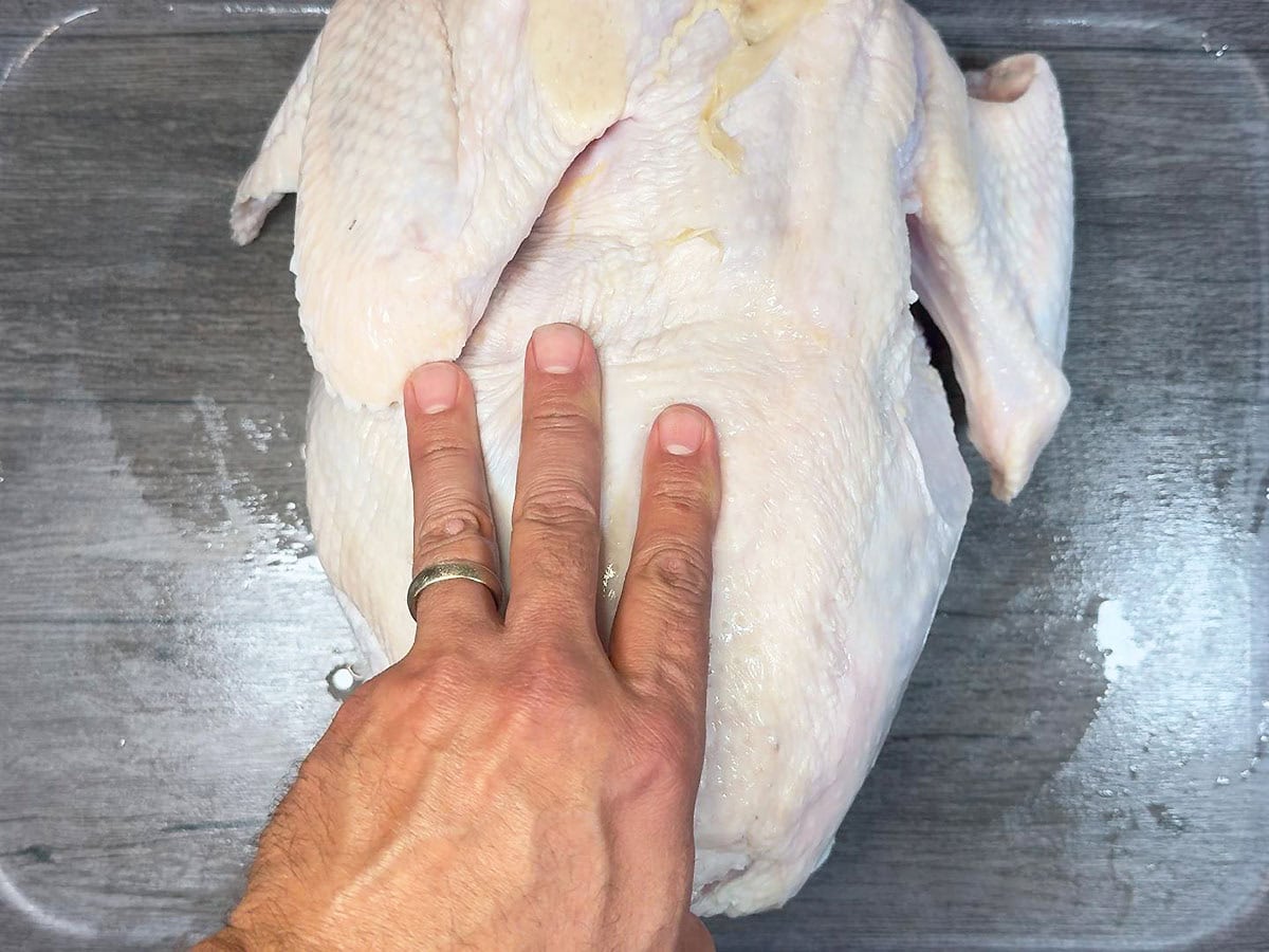 Turning an uncooked raw turkey over so the backbone is facing up.