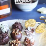 Seven decorated bourbon balls on a decorative plate with a set of tongs for serving.