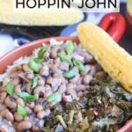 Red bowl with a handle filled with rice, Hoppin' John and greens. A pan of cornbread and hot sauce is in the background.