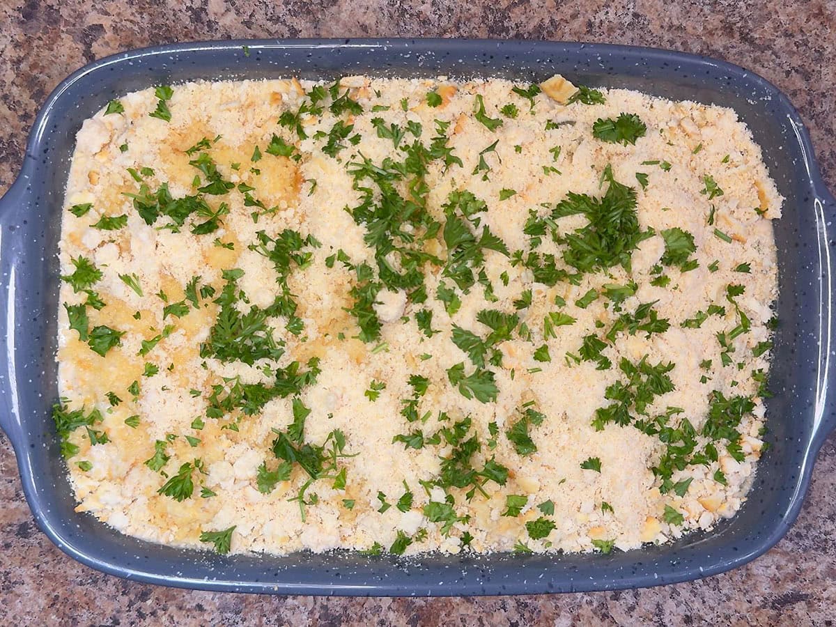 Unbaked scalloped oysters in a casserole dish topped with breadcrumbs, Parmesan cheese, and parsley.