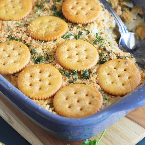 Scalloped oysters topped with Ritz crackers in a casserole dish with one serving removed.