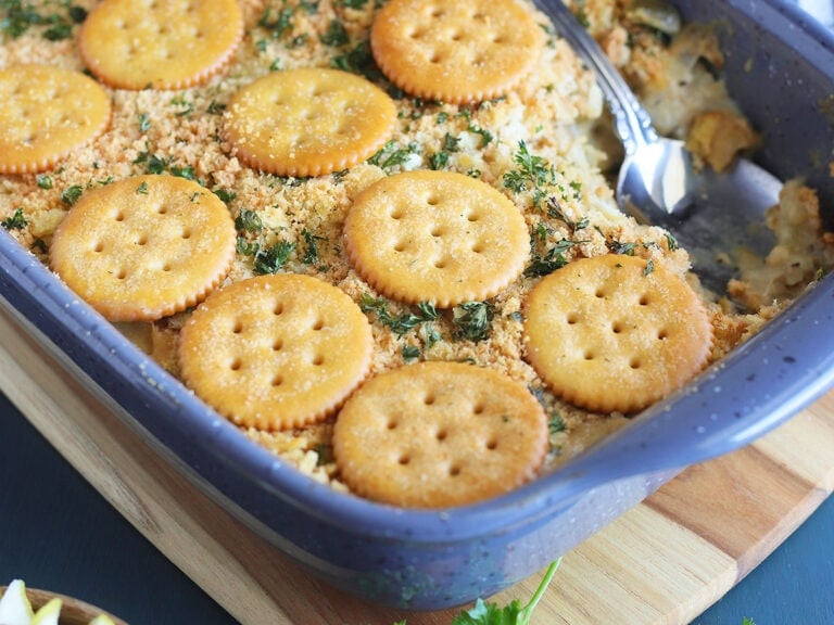 Scalloped oysters topped with Ritz crackers in a casserole dish with one serving removed.