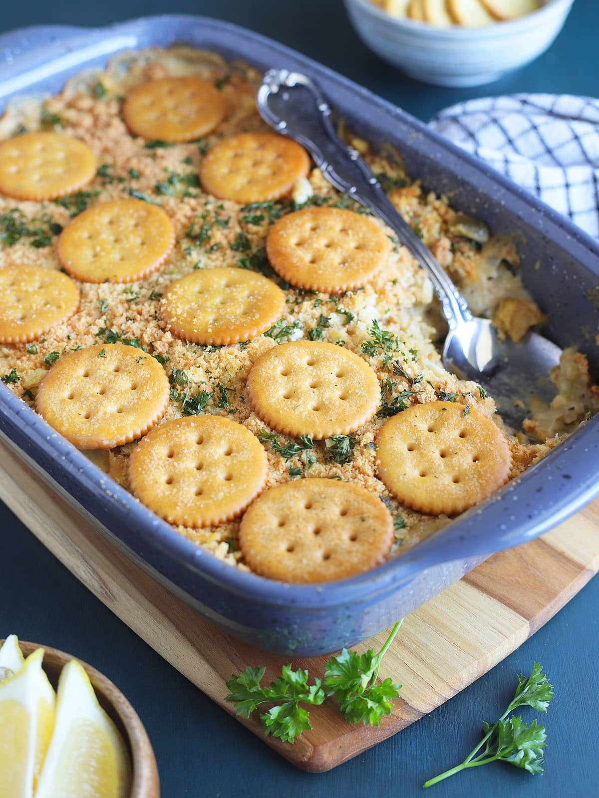 Scalloped oysters topped with Ritz crackers in a casserole dish with one serving removed.