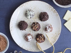 Seven decorated bourbon balls on a decorative plate with a set of tongs for serving.