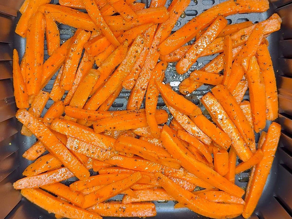Uncooked carrots spread in a single layer in an air fryer basket.