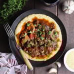 Bowl of grillades and grits garnished with chopped fresh parsley.