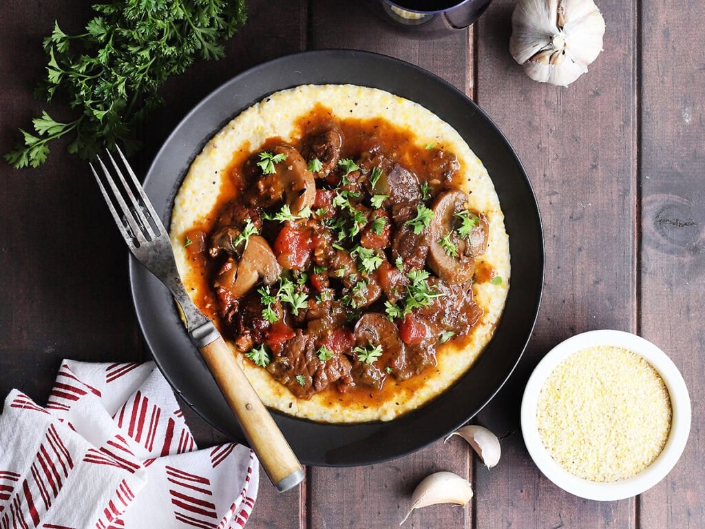Bowl of grillades and grits garnished with chopped fresh parsley.